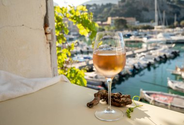 Soğuk gül şarabı, cam içinde sunulan güneş ışığı eşliğinde açık terasta, Cassis, Provence, Fransa 'da eski balıkçıların limanında renkli teknelerle sunuluyor.