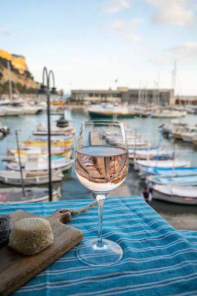 Açık terasta keçi peyniri ile servis edilen cam içinde Rose Provencal şarabı Cassis, Provence, Fransa 'da renkli teknelerle eski balıkçıların limanına bakıyor.