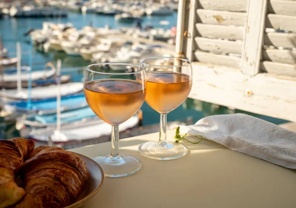 Soğuk gül Provencal şarabı bardaklarla sunuluyor. Açık terasta sunuluyor. Eski balıkçıların limanında, Cassis, Provence, Fransa 'da renkli tekneleri var.