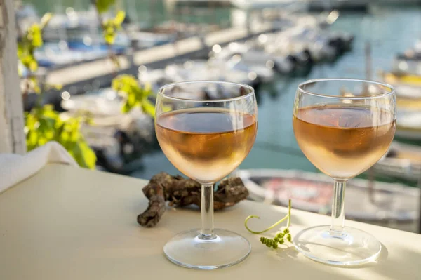 Soğuk gül Provencal şarabı bardaklarla sunuluyor. Açık terasta sunuluyor. Eski balıkçıların limanında, Cassis, Provence, Fransa 'da renkli tekneleri var.