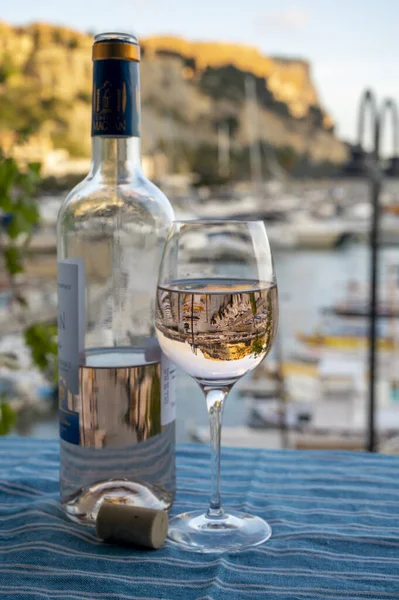 Rose Provencal şarabı cam ve şişeyle açık terasta eski balıkçıların limanı manzaralı Cassis, Provence, Fransa 'da renkli teknelerle servis ediliyor.