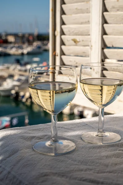 Cassis şaraplarından elde edilen iki bardak beyaz şarap, Fransa, Provence, Cassis 'te renkli tekneli eski balıkçıların limanı manzaralı terasta servis edilir.