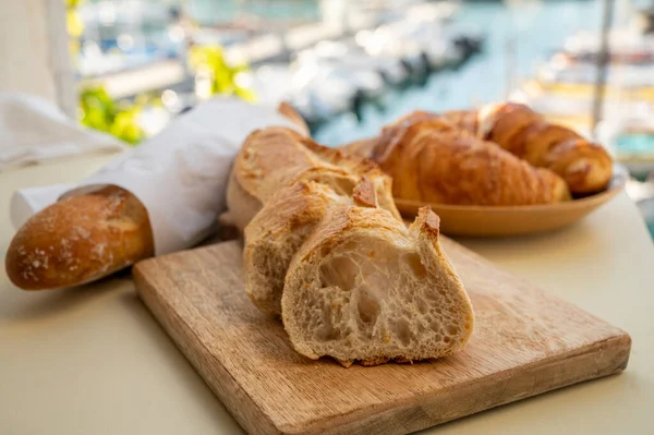 Provence 'de yaz sabahı, taze kruvasan ve baget ekmeği ile geleneksel kahvaltı Cassis, Provence, Fransa Limanı' ndaki balıkçı teknelerinin manzarası.
