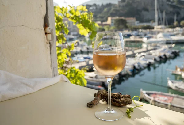 Soğuk gül şarabı, cam içinde sunulan güneş ışığı eşliğinde açık terasta, Cassis, Provence, Fransa 'da eski balıkçıların limanında renkli teknelerle sunuluyor.