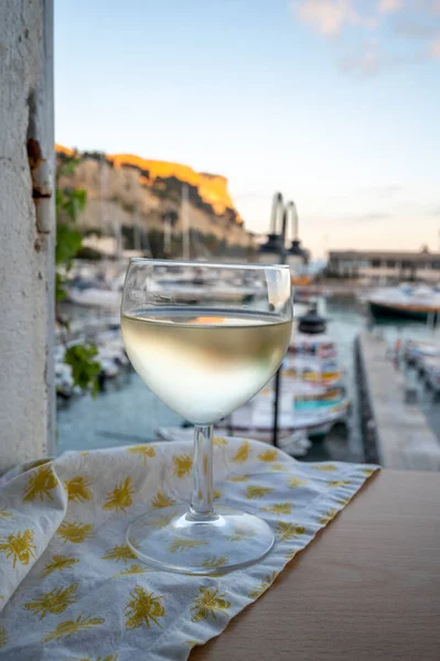 Cassis şarap üretim bölgesinden gelen soğuk beyaz şarap, Fransa, Provence, Cassis 'te renkli tekneleri olan eski balıkçıların limanına bakan terastaki camlarda servis edilir.