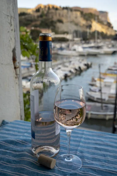 Rose Provencal şarabı cam ve şişeyle açık terasta eski balıkçıların limanı manzaralı Cassis, Provence, Fransa 'da renkli teknelerle servis ediliyor.