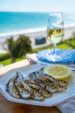 Sardalyalar şişler ve şöminede zeytin ağaçlarıyla hazırlandı, limon ve bir bardak sonlu şarapla servis edildi ve mavi deniz manzaralı, Malaga, Endülüs, İspanya 'da yaz tatili