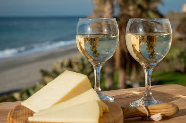 İspanyol sert manchegosu, inek, koyun ve keçi peyniri güneşli bir günde açık havada beyaz şarap ve mavi deniz manzarasıyla servis edilir.