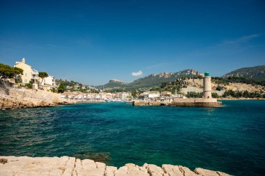 Kumsalda panoramik manzara, mavi deniz, uçurumlar, evler, sokaklar ve bulutlu bir günde Cassis, Provence, Fransa 'da deniz feneriyle eski balıkçıların limanı