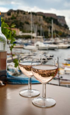 Açık terasta sunulan Rose Provencal şarabı Cassis, Provence, Fransa 'da renkli tekneleri olan eski balıkçıların limanına bakıyor.