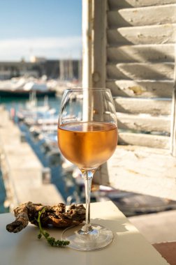 Soğuk gül şarabı, cam içinde sunulan güneş ışığı eşliğinde açık terasta, Cassis, Provence, Fransa 'da eski balıkçıların limanında renkli teknelerle sunuluyor.