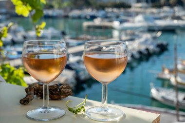Soğuk gül Provencal şarabı bardaklarla sunuluyor. Açık terasta sunuluyor. Eski balıkçıların limanında, Cassis, Provence, Fransa 'da renkli tekneleri var.