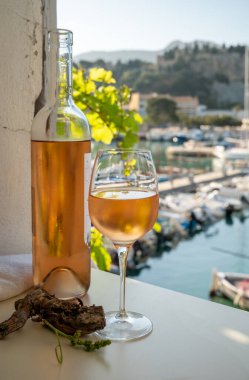 Soğuk gül, cam ve şişe Provencal şarabı. Açık terasta güneş ışığında servis ediliyor. Eski balıkçıların limanında, Cassis, Provence, Fransa 'da renkli tekneleri var.