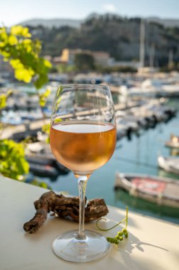 Soğuk gül şarabı, cam içinde sunulan güneş ışığı eşliğinde açık terasta, Cassis, Provence, Fransa 'da eski balıkçıların limanında renkli teknelerle sunuluyor.