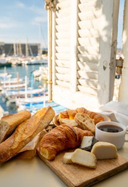 Fransız kahvaltısında taze kruvasan, baquett ekmeği, crottin keçi peyniri, sade kahve ve Cassis, Provence, Fransa 'daki balıkçı tekneleri manzaralı. Provence 'de Tatil.