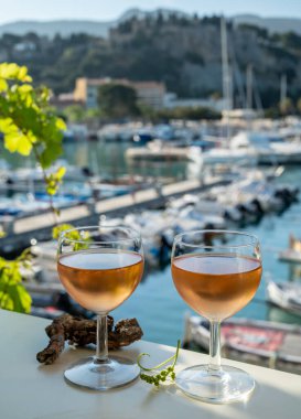 Soğuk gül Provencal şarabı bardaklarla sunuluyor. Açık terasta sunuluyor. Eski balıkçıların limanında, Cassis, Provence, Fransa 'da renkli tekneleri var.
