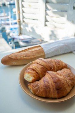 Provence 'de yaz sabahı, taze kruvasan ve baget ekmeği ile geleneksel kahvaltı Cassis, Provence, Fransa Limanı' ndaki balıkçı teknelerinin manzarası.