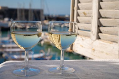 Cassis şaraplarından elde edilen iki bardak beyaz şarap, Fransa, Provence, Cassis 'te renkli tekneli eski balıkçıların limanı manzaralı terasta servis edilir.