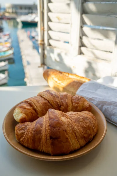 Provence 'de yaz sabahı, taze kruvasan ve baget ekmeği ile geleneksel kahvaltı Cassis, Provence, Fransa Limanı' ndaki balıkçı teknelerinin manzarası.