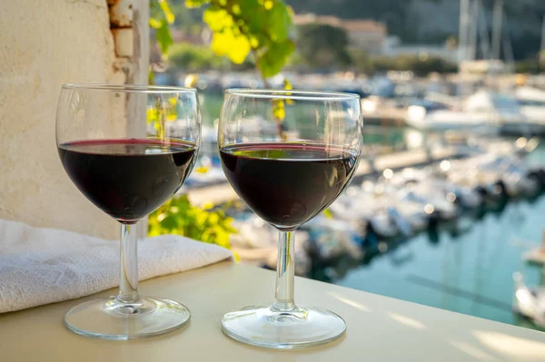 Drinking of red dry wine on outdoor terrace with view on old fisherman's harbour with colourful boats in Cassis, Provence, France