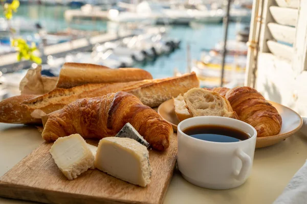 Fransız kahvaltısında taze kruvasan, baquett ekmeği, crottin keçi peyniri, sade kahve ve Cassis, Provence, Fransa 'daki balıkçı tekneleri manzaralı. Provence 'de Tatil.