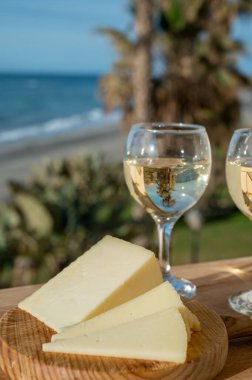 İspanyol sert manchegosu, inek, koyun ve keçi peyniri güneşli bir günde açık havada beyaz şarap ve mavi deniz manzarasıyla servis edilir.