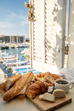 Fransız kahvaltısında taze kruvasan, baquett ekmeği, crottin keçi peyniri, sade kahve ve Cassis, Provence, Fransa 'daki balıkçı tekneleri manzaralı. Provence 'de Tatil.