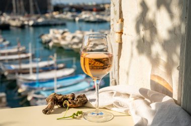 Soğuk gül şarabı, cam içinde sunulan güneş ışığı eşliğinde açık terasta, Cassis, Provence, Fransa 'da eski balıkçıların limanında renkli teknelerle sunuluyor.