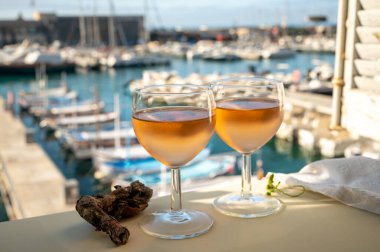 Soğuk gül Provencal şarabı bardaklarla sunuluyor. Açık terasta sunuluyor. Eski balıkçıların limanında, Cassis, Provence, Fransa 'da renkli tekneleri var.