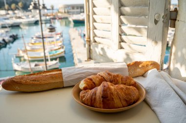 Provence 'de yaz sabahı, taze kruvasan ve baget ekmeği ile geleneksel kahvaltı Cassis, Provence, Fransa Limanı' ndaki balıkçı teknelerinin manzarası.