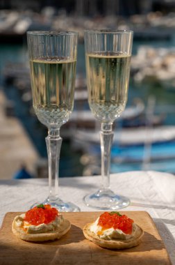 Ekşi krema ve tuzlu somon kırmızısı havyar ve Fransız şampanyası brut köpüklü şarap ile küçük krep çiftleri Cassis, Provence, Fransa 'nın limanındaki renkli teknelerde servis edilir.