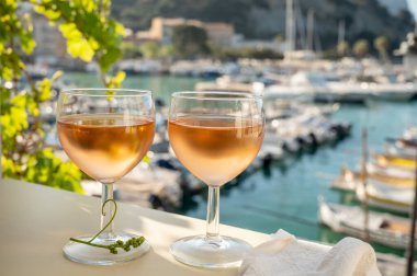 Soğuk gül Provencal şarabı bardaklarla sunuluyor. Açık terasta sunuluyor. Eski balıkçıların limanında, Cassis, Provence, Fransa 'da renkli tekneleri var.