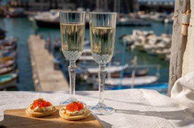 Ekşi krema ve tuzlu somon kırmızısı havyar ve Fransız şampanyası brut köpüklü şarap ile küçük krep çiftleri Cassis, Provence, Fransa 'nın limanındaki renkli teknelerde servis edilir.