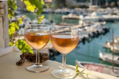 Soğuk gül Provencal şarabı bardaklarla sunuluyor. Açık terasta sunuluyor. Eski balıkçıların limanında, Cassis, Provence, Fransa 'da renkli tekneleri var.