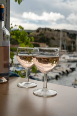 Açık terasta sunulan Rose Provencal şarabı Cassis, Provence, Fransa 'da renkli tekneleri olan eski balıkçıların limanına bakıyor.