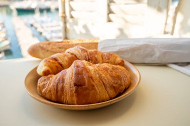 Provence 'de yaz sabahı, taze kruvasan ve baget ekmeği ile geleneksel kahvaltı Cassis, Provence, Fransa Limanı' ndaki balıkçı teknelerinin manzarası.