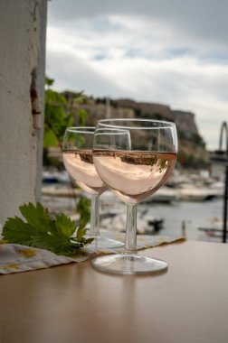 Açık terasta sunulan Rose Provencal şarabı Cassis, Provence, Fransa 'da renkli tekneleri olan eski balıkçıların limanına bakıyor.