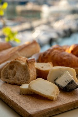 Provence 'de güneşli bir sabah, taze kruvasan, baquett ekmeği, crottin keçi peyniri ve Cassis, Provence, Fransa limanındaki balıkçı tekneleri manzaralı bir kahvaltı.