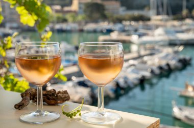 Soğuk gül Provencal şarabı bardaklarla sunuluyor. Açık terasta sunuluyor. Eski balıkçıların limanında, Cassis, Provence, Fransa 'da renkli tekneleri var.