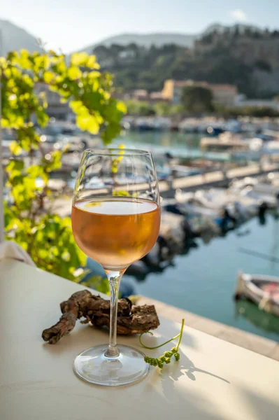 Soğuk gül şarabı, cam içinde sunulan güneş ışığı eşliğinde açık terasta, Cassis, Provence, Fransa 'da eski balıkçıların limanında renkli teknelerle sunuluyor.
