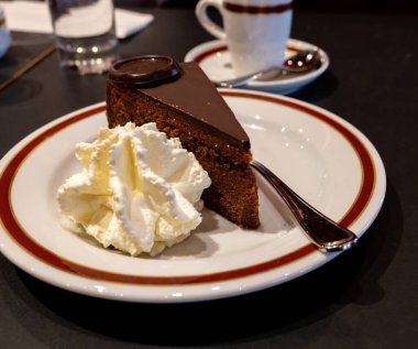 Meşhur Sachertorte çikolatalı pastası. Kayısı reçeli ve beyaz tahtada krem şanti ile servis ediliyor.