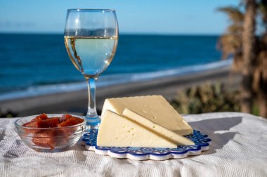 İspanyol sert keçi peyniri, açık havada membrillo reçeli ve arka planda mavi deniz bulunan bir bardak beyaz şarapla servis edilir.