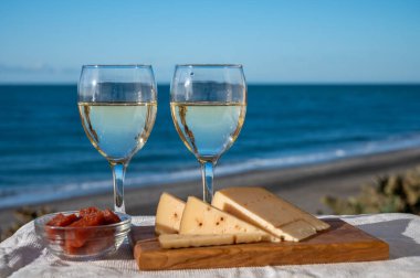 İspanyol sert Endülüs peyniri tatlı şeri ile dolu açık havada servis edilen membrillo reçeli iki bardak beyaz şarap ve arka planda mavi deniz, yakın çekim.