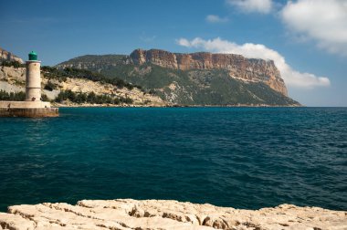 Kumsalda panoramik manzara, mavi deniz, uçurumlar, evler, sokaklar ve bulutlu bir günde Cassis, Provence, Fransa 'da deniz feneriyle eski balıkçıların limanı