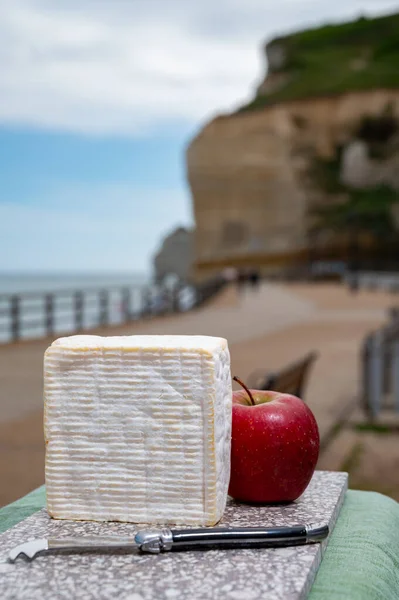 French squared pont l\'eveque cow cheese from Calvados department served outdoor with apple and view on alebaster cliffs of Porte d\'Aval in Etretat, Normandy, France