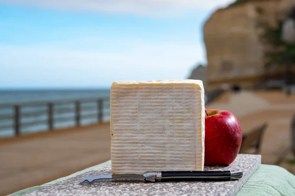 French squared pont l\'eveque cow cheese from Calvados department served outdoor with apple and view on alebaster cliffs of Porte d\'Aval in Etretat, Normandy, France