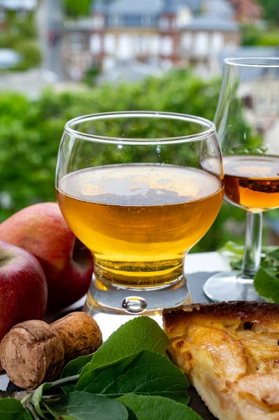 Apple products of Normandy region, homemade baked apple cake, glasses of calvados and cider drink and houses of Etretat village on background, Normandy, France