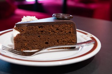 Meşhur Sachertorte çikolatalı pastası. Kayısı reçeli ve beyaz tahtada krem şanti ile servis ediliyor.