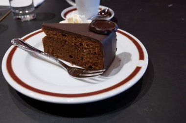 Meşhur Sachertorte çikolatalı pastası. Kayısı reçeli ve beyaz tahtada krem şanti ile servis ediliyor.