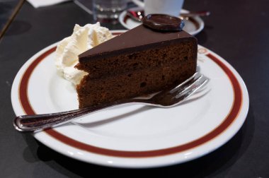 Meşhur Sachertorte çikolatalı pastası. Kayısı reçeli ve beyaz tahtada krem şanti ile servis ediliyor.